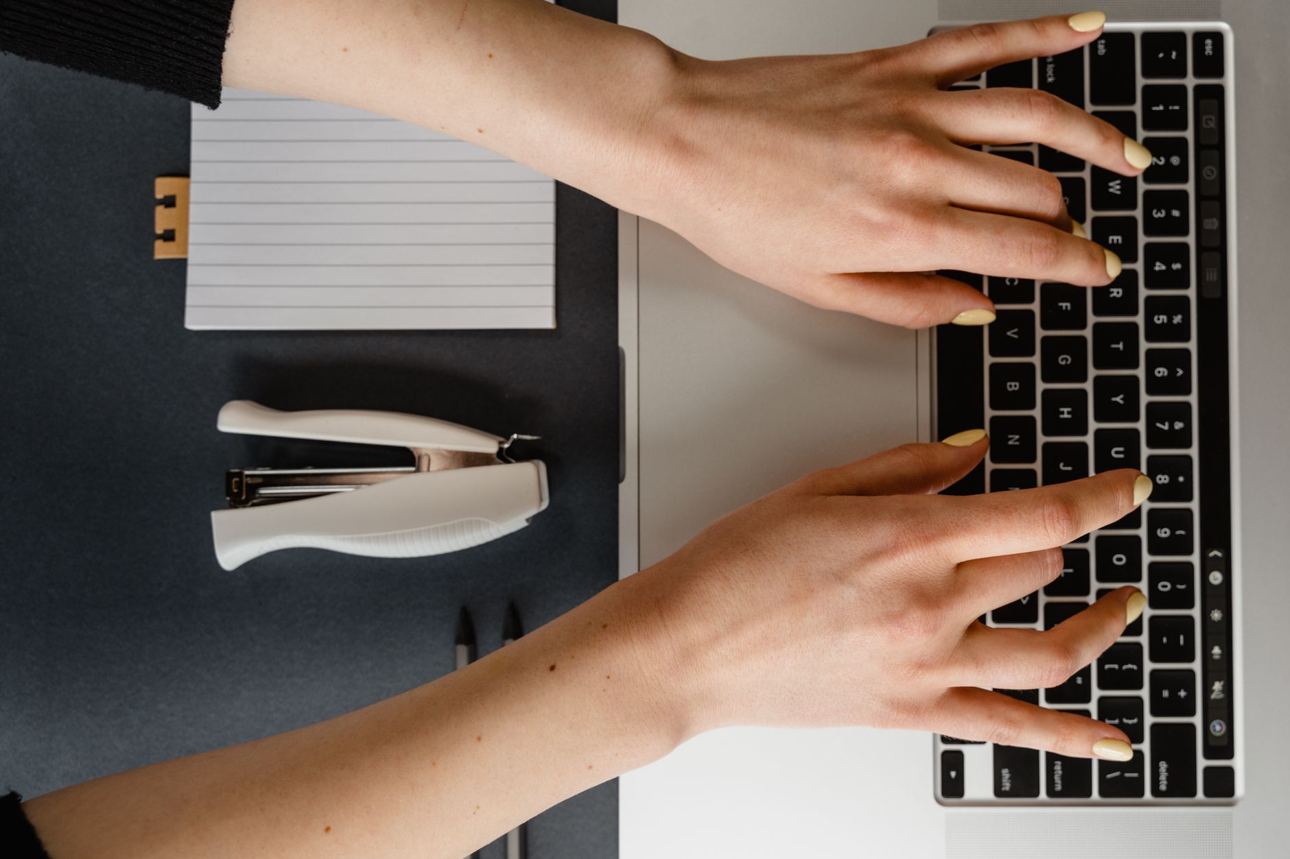 Dłonie piszące na laptopie przy biurku z przyborami biurowymi
